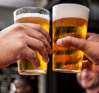 Close-up of two friends toasting with cold beer glasses at a lively bar, celebrating friendship and good times.